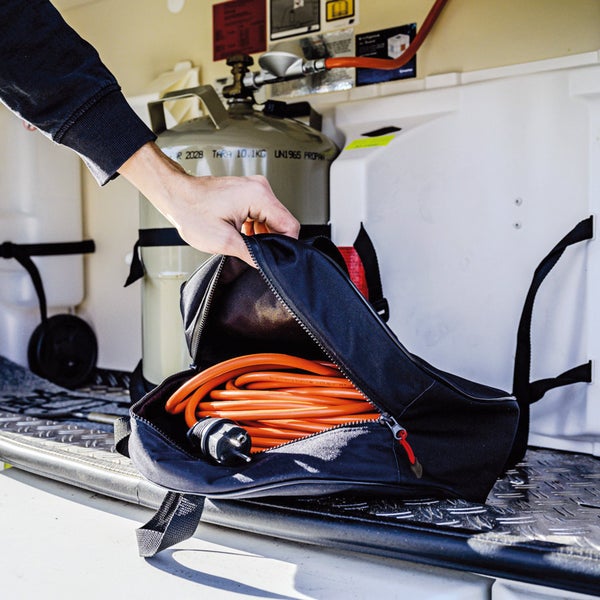 Eine Person öffnet eine schwarze Tasche mit einem orangefarbenen Kabel und einem Stecker darin