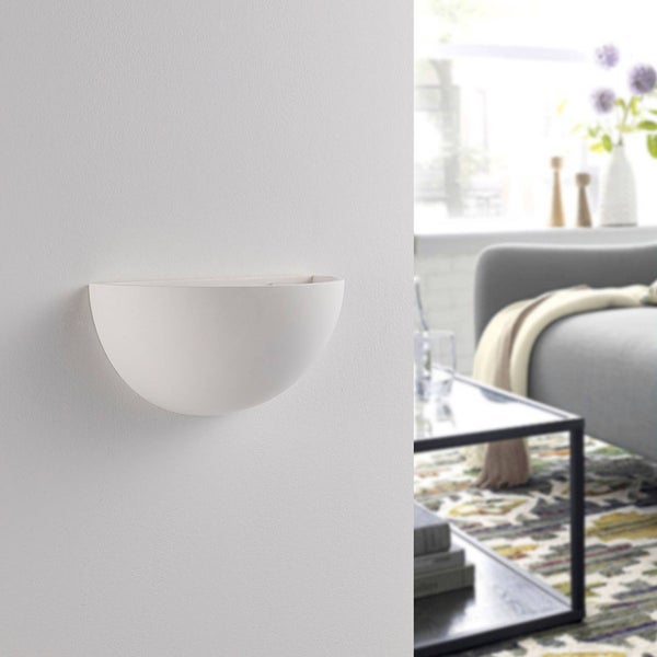 Weiße halbschalenförmige Wandleuchte aus Gips für indirekte Beleuchtung in einem hellen, modern eingerichteten Wohnzimmer mit Sofa und Tisch.