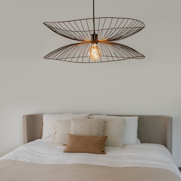 Draht-Pendelleuchte über einem Bett im Schlafzimmer.