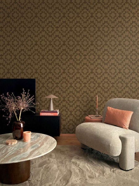 Wohnzimmer mit gemusterter Vliestapete, modernem Sessel, Couchtisch aus Stein und Dekoartikeln in einer behaglichen Inneneinrichtung.