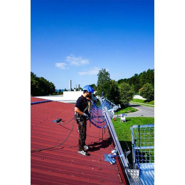 Ein Arbeiter mit Schutzhelm und Sicherheitsgurt installiert ein Schutznetz auf einem Dach.