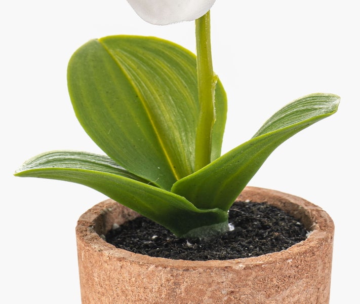Künstliche Orchidee im braunen Tontopf mit grünen Blättern und Stiel.