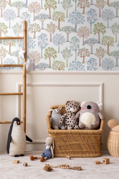 Kinderzimmer mit Tapete mit Baummotiv, Korbsessel mit Stofftieren, Holzleiter und Pinguin-Plüschtier auf hellem Teppich.