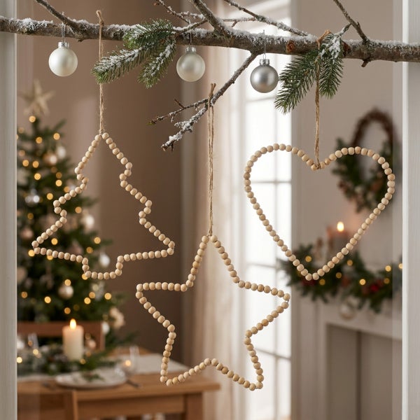 Weihnachtsdekoration Anhänger aus Holzperlen in Stern, Herz und Tannenbaumform hängen an einem verschneiten Ast mit Weihnachtskugeln.