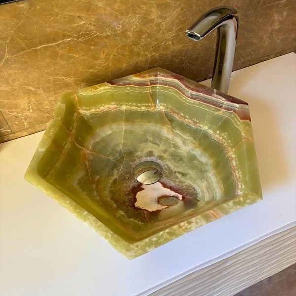 Hexagonales Aufsatzwaschbecken aus Onyx Naturstein mit verchromter Armatur auf einem Waschtisch vor einer Steinwand.