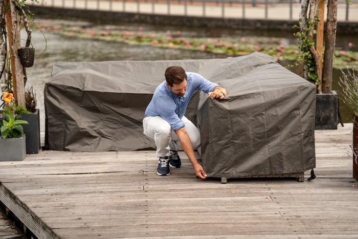 Mann befestigt Schutzhülle über Gartenmöbeln auf einer Holzterrasse