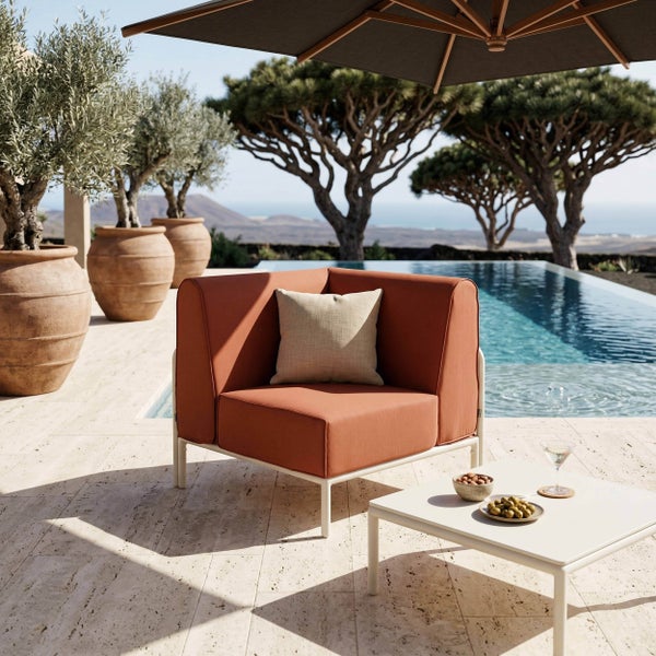 Modernes Outdoor-Lounge-Set mit rostfarbenem Ecksessel und weißem Metalltisch auf einer hellen Steinterrasse an einem Pool in sonniger Atmosphäre.