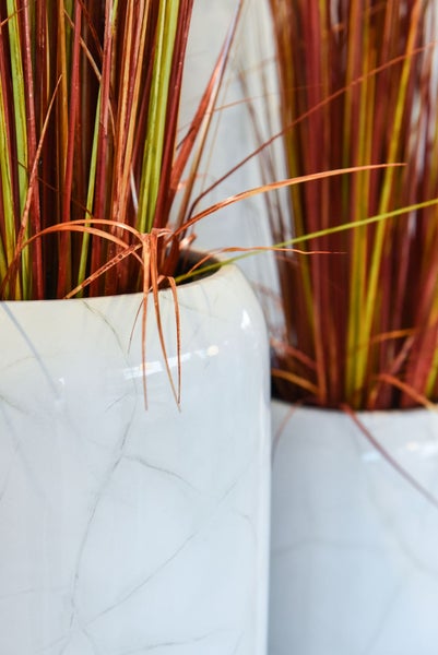 Nahaufnahme einer weißen Keramikvase mit Marmor-Optik und rötlichem Dekogras.