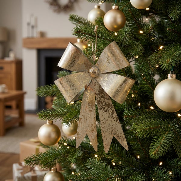 Dekorative Weihnachtsbaumschleife in rustikaler Metalloptik als Christbaumschmuck in einem geschmückten Wohnzimmer.