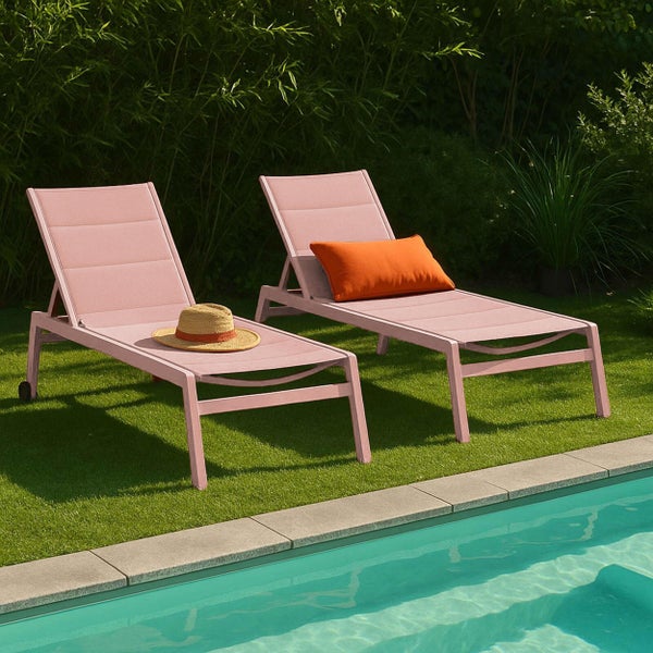 Zwei rosa Sonnenliegen mit verstellbarer Rückenlehne auf einer Rasenfläche am Pool, dekoriert mit Strohhut und orangefarbenem Kissen.