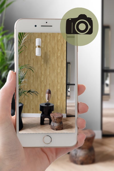 Aufnahme eines Raumes mit gemusterter Tapete, Leuchte und Dekoration, betrachtet durch ein Smartphone.