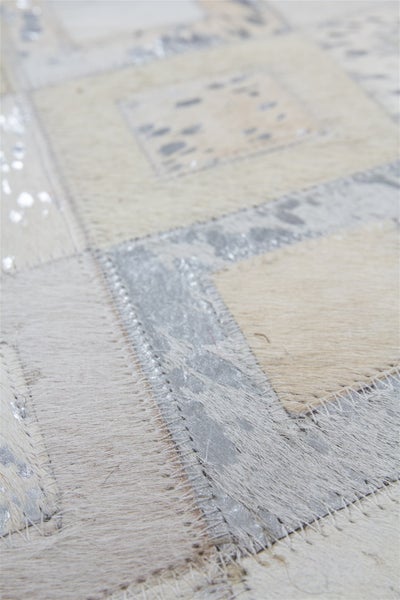 Detailaufnahme eines Patchwork-Kuhfellteppichs mit cremefarbenen und silbernen Abschnitten sowie sichtbaren Nähten.