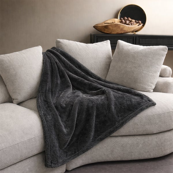 Eine weiche Wohndecke auf einem modernen Sofa mit Kissen in einem wohnlichen Wohnzimmer.