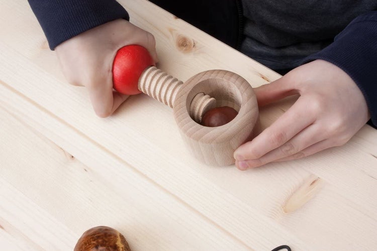 Ein hölzerner Nussknacker in Schraubmechanik Form wird von Händen bedient um eine Kastanie zu knacken.