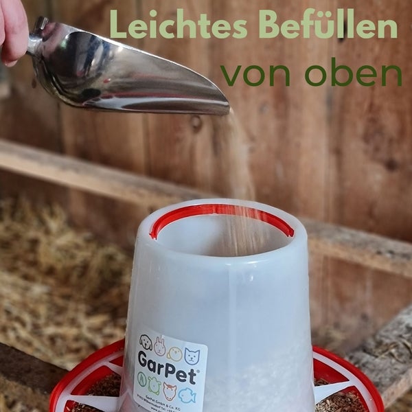 Befüllen eines Kunststoff Futterspenders für Geflügel von oben mit einer Metallschaufel.