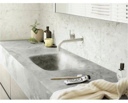 Modernes Badezimmer mit integriertem Waschbecken in einer grauen Arbeitsplatte, Wandarmatur und hellen Natursteinfliesen.