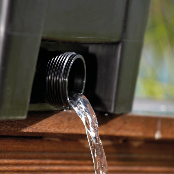 Wasser fließt aus dem Gewindeanschluss eines grünen Regenfasses aus Kunststoff auf Holz.