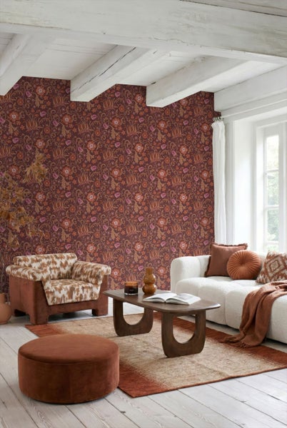 Wohnzimmer mit floraler Tapete in Dunkelrot und Orange, weißem Sofa, gemustertem Sessel und Holzcouchtisch in warmen Erdtönen.