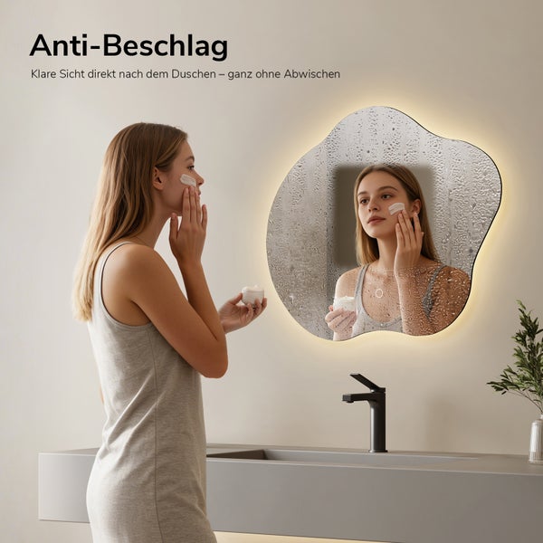 Organisch geformter LED-Badspiegel mit Anti-Beschlag-Funktion im modernen Badezimmer mit grauem Waschtisch, Frau vor klarem Spiegelbild.