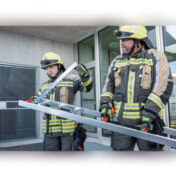 Zwei Feuerwehrleute tragen eine Aluminiumleiter vor einem Gebäude