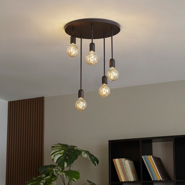 Moderne Deckenleuchte mit fünf Pendelleuchten und Filament-Leuchtmitteln in unterschiedlichen Höhen in einem Wohnzimmer.
