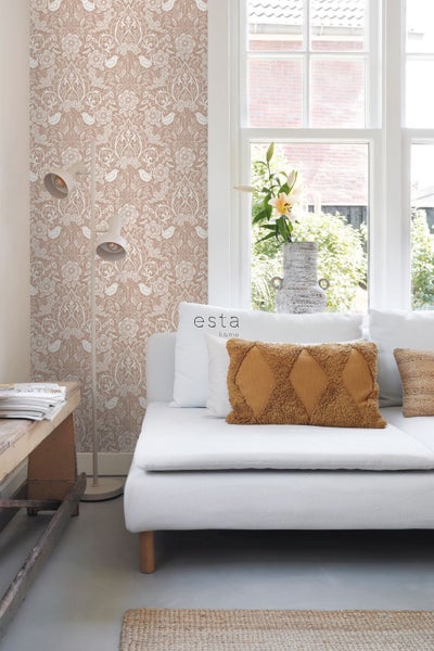 Vliestapete mit floralem Muster und Vögeln in einem hellen Wohnzimmer mit Sofa, Kissen, Stehlampe und Fenster.