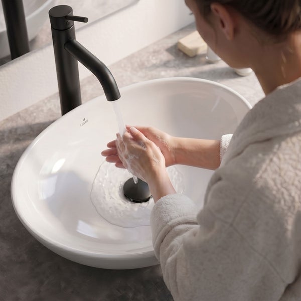 Person wäscht sich die Hände in einem weißen Aufsatzwaschbecken mit einer hohen schwarzen Armatur in einem modernen Badezimmer.