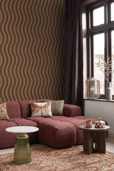 Wohnzimmer mit brauner Wellentapete an der Wand, einem roten modularen Sofa und zwei Beistelltischen.