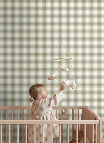 Vliestapete mit Vichy-Karo-Muster in einem hellen Kinderzimmer mit Babybett aus Holz und Mobile.