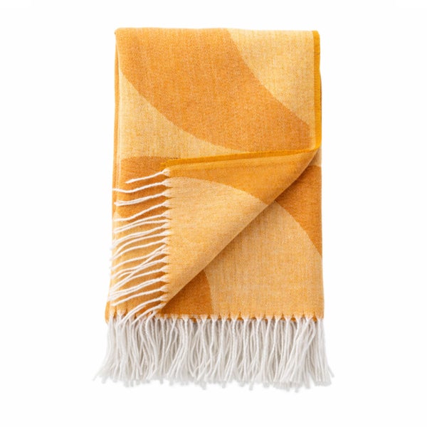 Gefaltete Wohndecke mit gelb-orangem Wellenmuster und weißen Fransen.