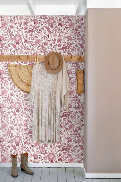 Wohnraum mit floraler Mustertapete, Holzgarderobe mit Kleid, Hut und Stiefeln im Eingangsbereich.
