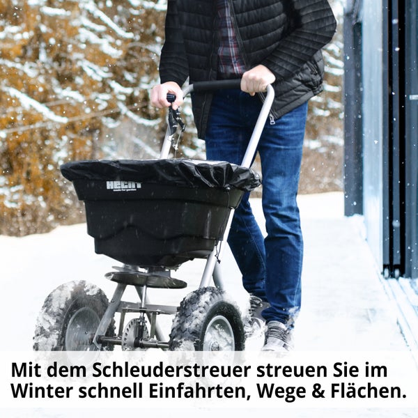 Person schiebt Streuwagen auf verschneitem Weg