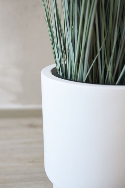 Künstliches Gras in einem weißen zylindrischen Blumentopf.
