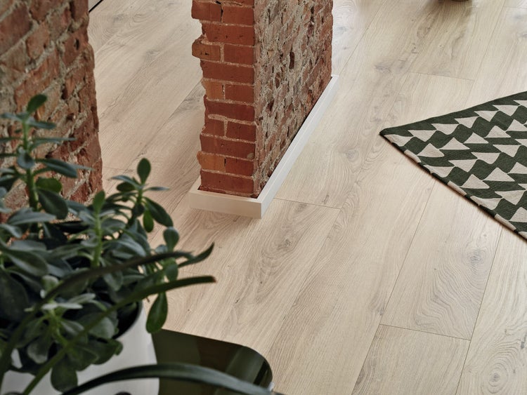 Wohnraum mit Eichenholzoptik Laminatboden kombiniert mit einer Ziegelsteinmauer und einer Grünpflanze.