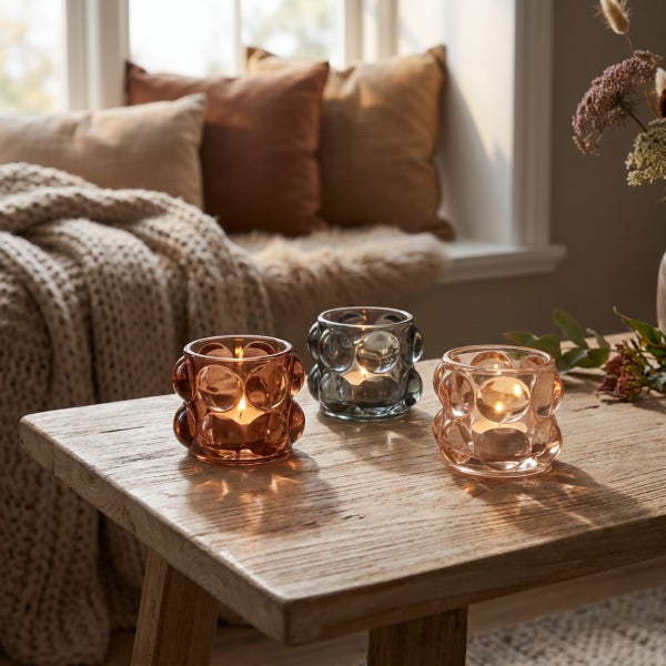 Drei kleine Windlichter aus Glas mit Noppenstruktur stehen auf einem Holztisch, ein brennendes Teelicht in jedem Glas.