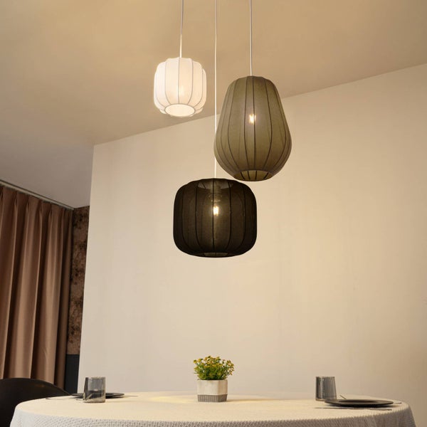 Drei Pendelleuchten mit gerippten Stoffschirmen in verschiedenen Formen über einem gedeckten runden Esstisch in einem hellen Raum.