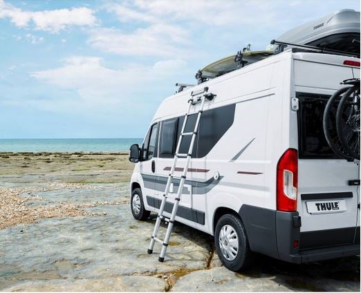 Weißer Kastenwagen mit Dachbox, Leiter und Fahrradträger am Strand