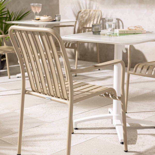 Gartenmöbel-Set mit beigen Metallstühlen im Latten-Design und weißen Bistrotischen auf einer hellen Terrasse.