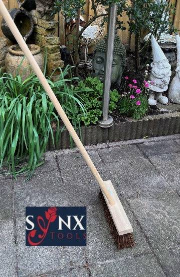 Bürste mit Holzstiel auf Pflastersteinen im Garten