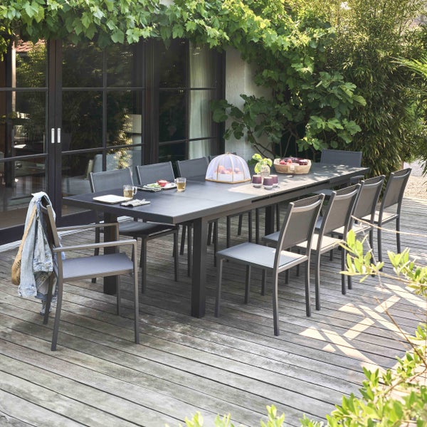 Moderne Garten-Essgruppe mit großem Tisch und Stühlen auf einer Holzterrasse, umgeben von Pflanzen.