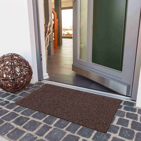 Braune Fußmatte vor einer offenen Haustür auf Pflastersteinen