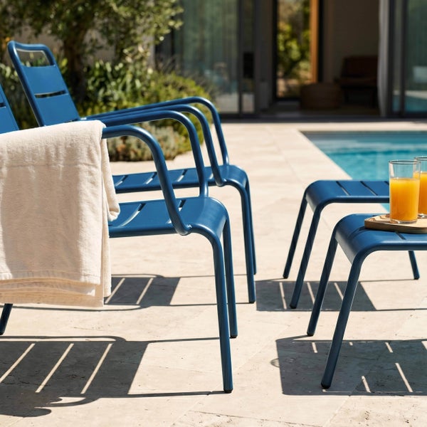 Moderne Gartenstühle und Hocker aus Metall auf einer sonnigen Terrasse am Pool mit einem Handtuch und Saftgläsern.