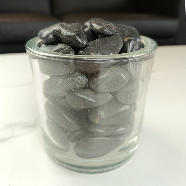 Dunkle glatte Dekosteine in einem transparenten Glasgefäß für die Innenraumgestaltung.