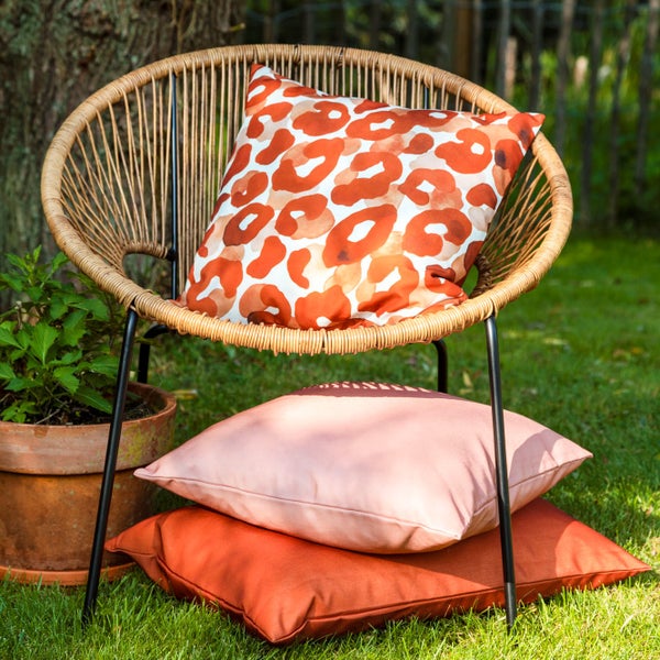 Rattan Sessel mit gemustertem Kissen und zwei weiteren Kissen auf dem Rasen