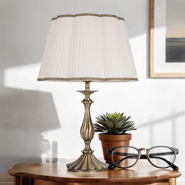 Tischleuchte mit plissiertem Schirm, Dekoration, Zimmerpflanze und Brille auf einem Tisch