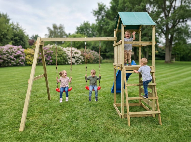 Spielturm aus Holz im Garten mit zwei Schaukeln, blauer Rutsche und Klettergerüst mit grünem Dach. Kinder spielen auf der hellen, gepflegten Anlage.