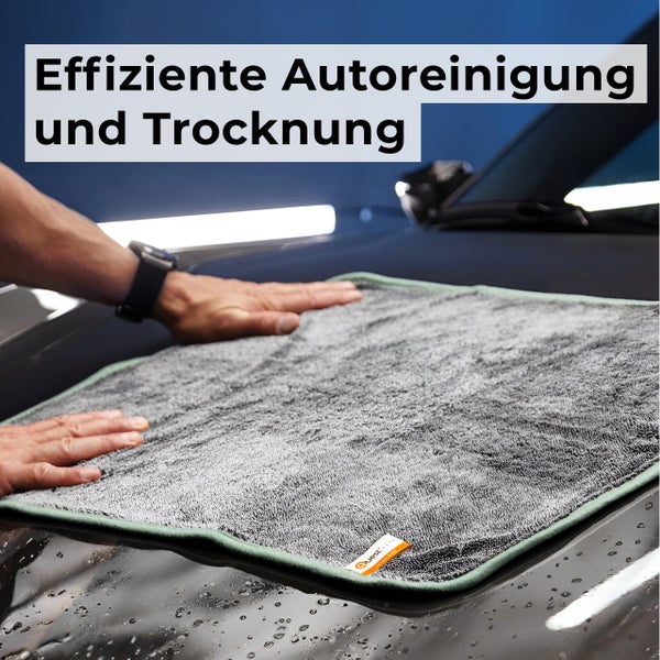 Ein großes Mikrofasertuch wird zur effizienten Autoreinigung und Trocknung flach auf die nasse Motorhaube eines Autos gelegt.