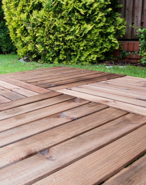Terrassenfliesen aus Holz im Garten auf einer Rasenfläche verlegt, unterschiedliche Behandlungsstufen der Oberfläche sichtbar.