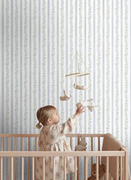 Kinderzimmertapete mit vertikalen Streifen und floralen Mustern hinter einem Kind in einem Gitterbett.