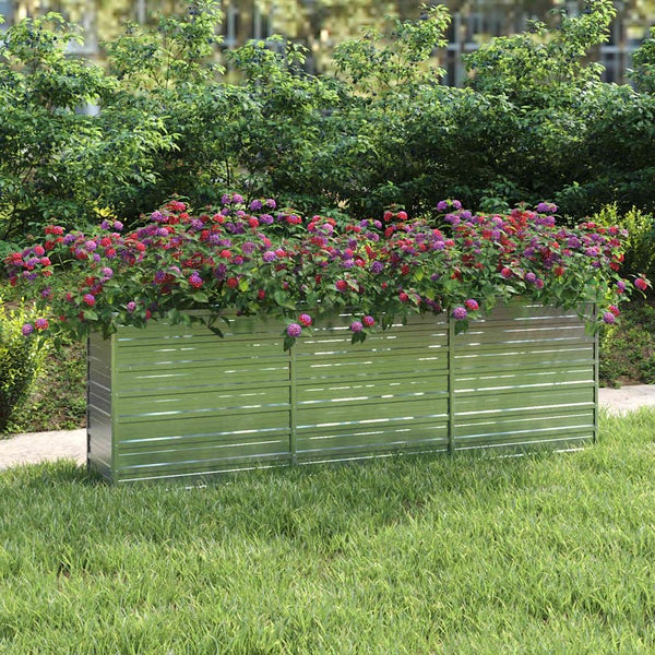Rechteckiges Hochbeet aus Metall mit horizontaler Wellenstruktur, bepflanzt mit Blumen auf einer Rasenfläche vor einer Hecke.